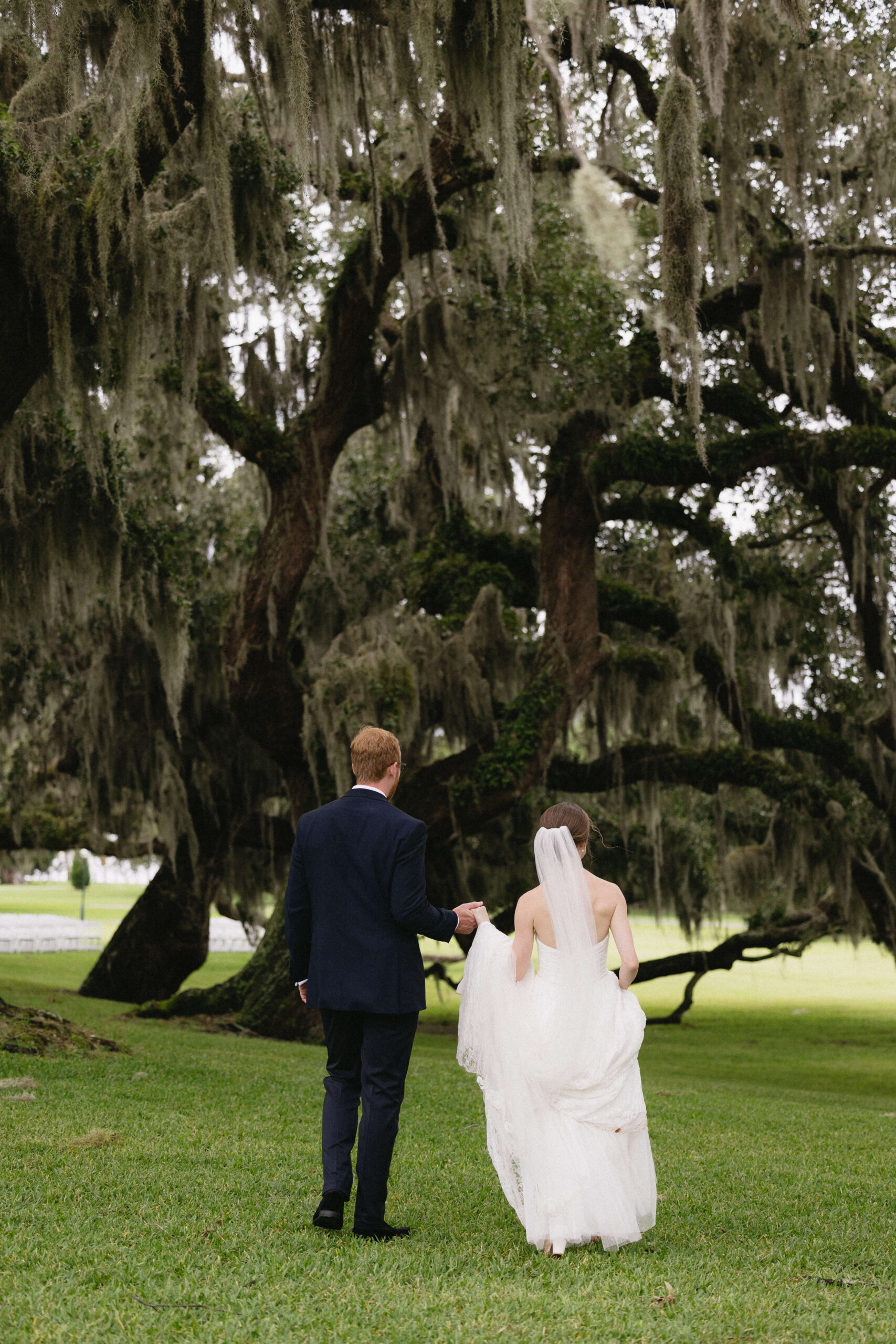 bride and groom walking away under oak trees at jekyll island wedding
