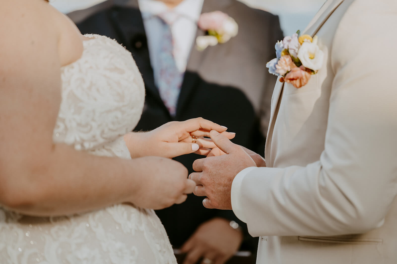 close up of bride and groom putting wedding rings on