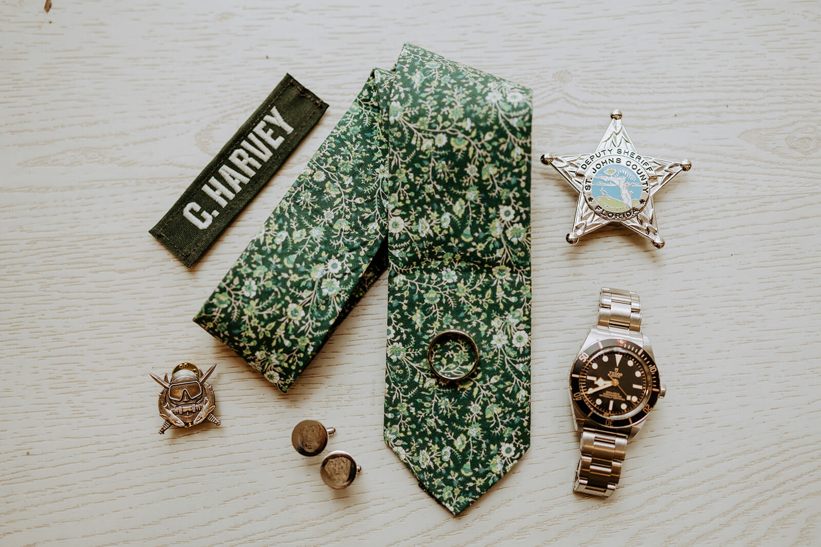 detail image of grooms watch, cufflinks, and floral green tie