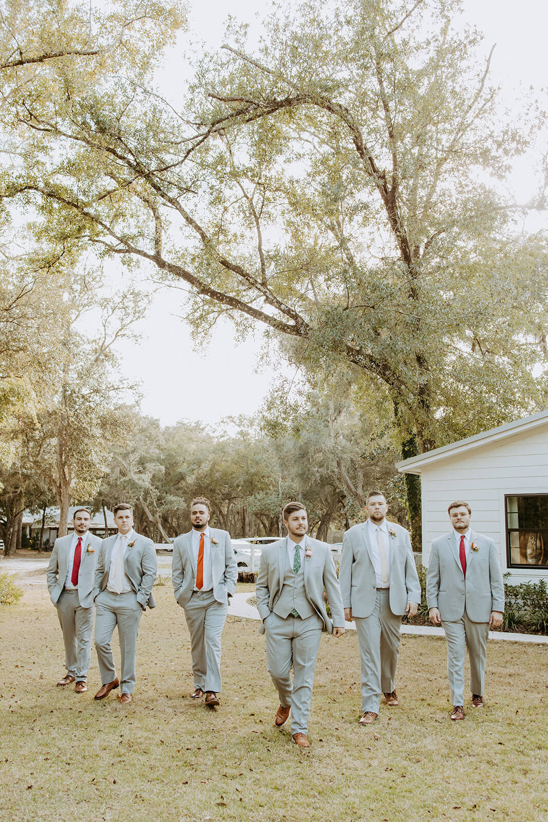 Groom walking with his groomsmen under large trees