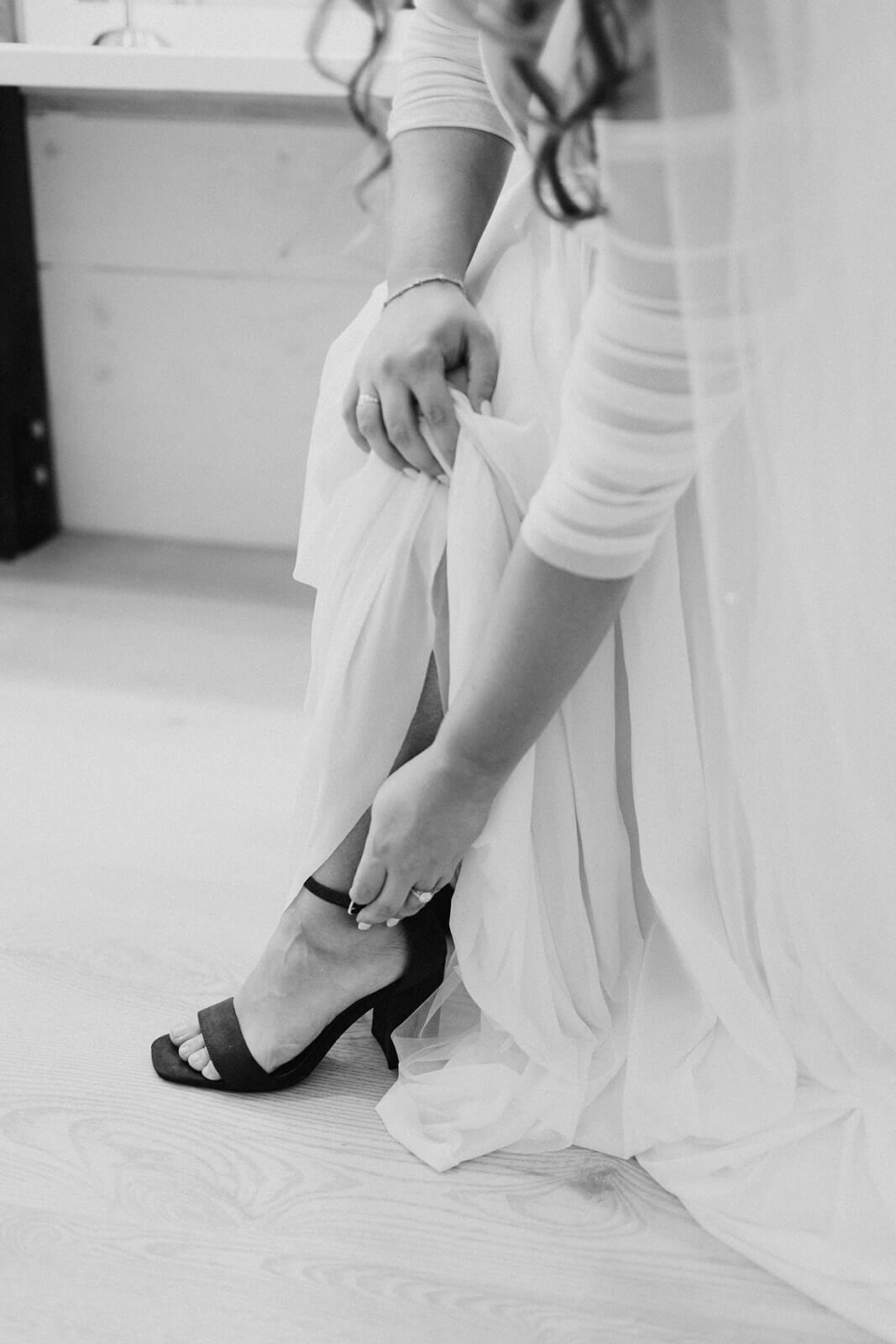 close up image of bride putting on black high heels