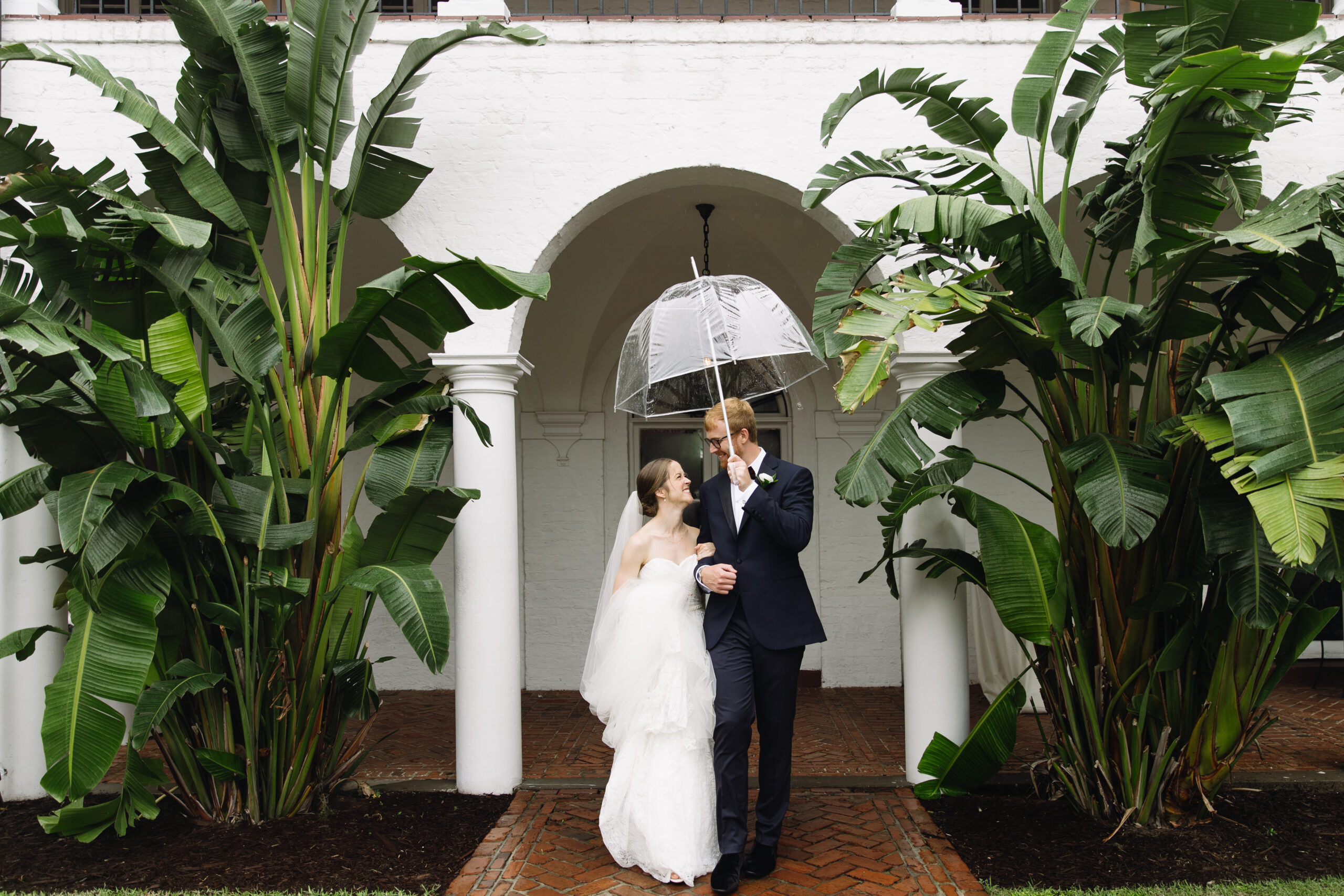 Bride and groom walk together while carrying umbrella